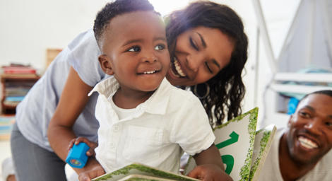 Mum and Dad smiling and hugging a young boy that is reading a book about numbers.