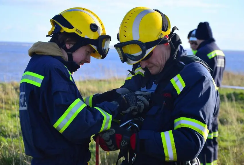Two firefighters help each other put on specialist harnesses