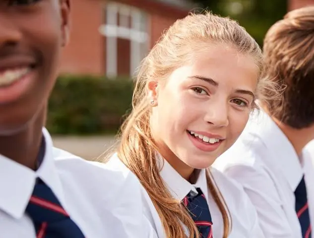 Teenage girl in school uniform sitting with other pupils outside and smiling