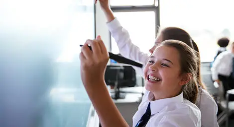 Two school children write on aboard in a classroom