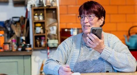 Woman over 50 talking on the phone while writing in her home kitchen
