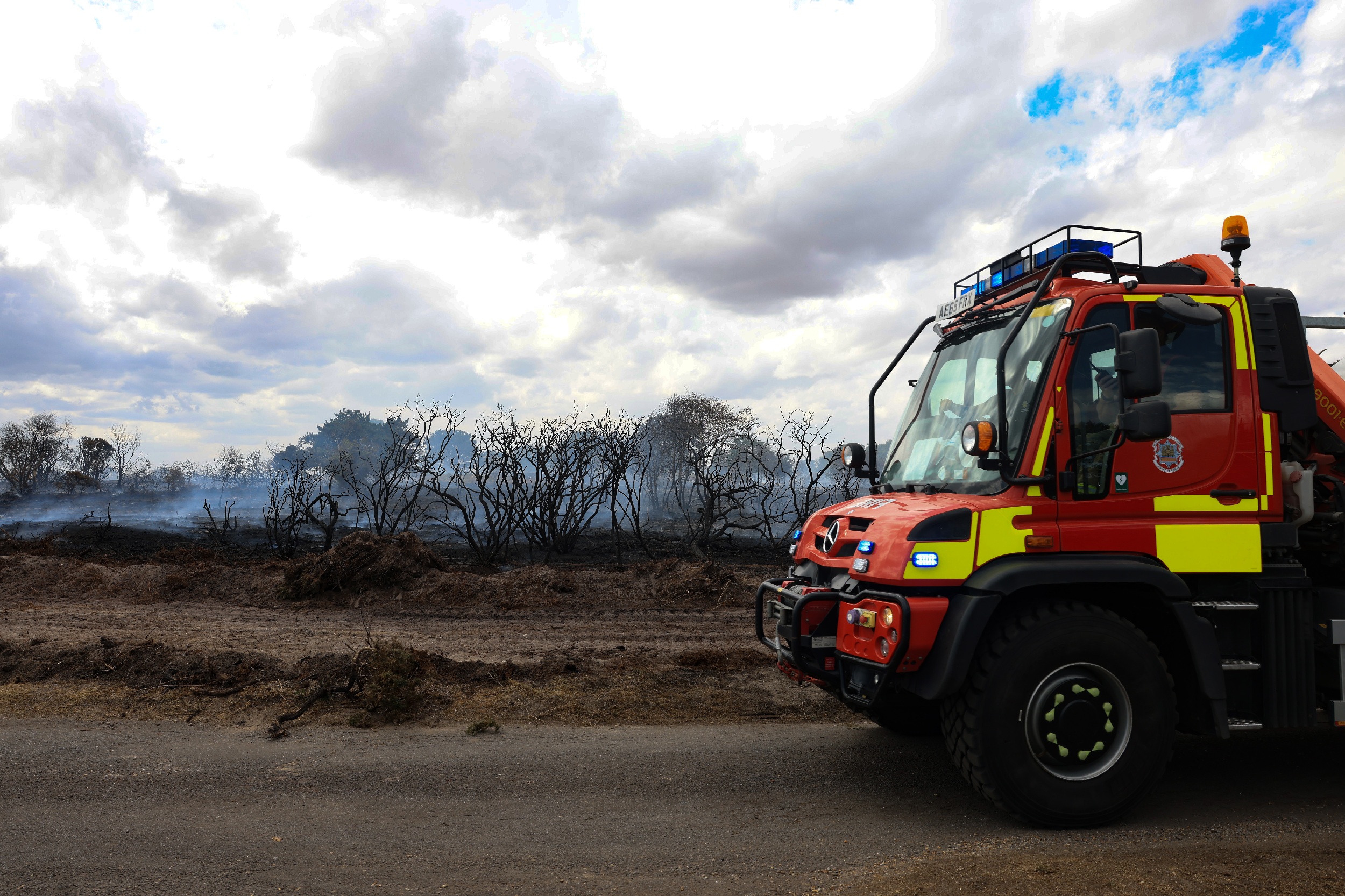 a unimog fire appliance parked in front of burned out heathland and forest