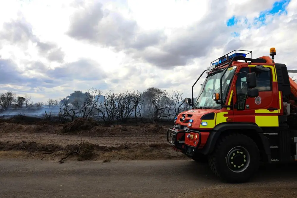 a unimog fire appliance parked in front of burned out heathland and forest