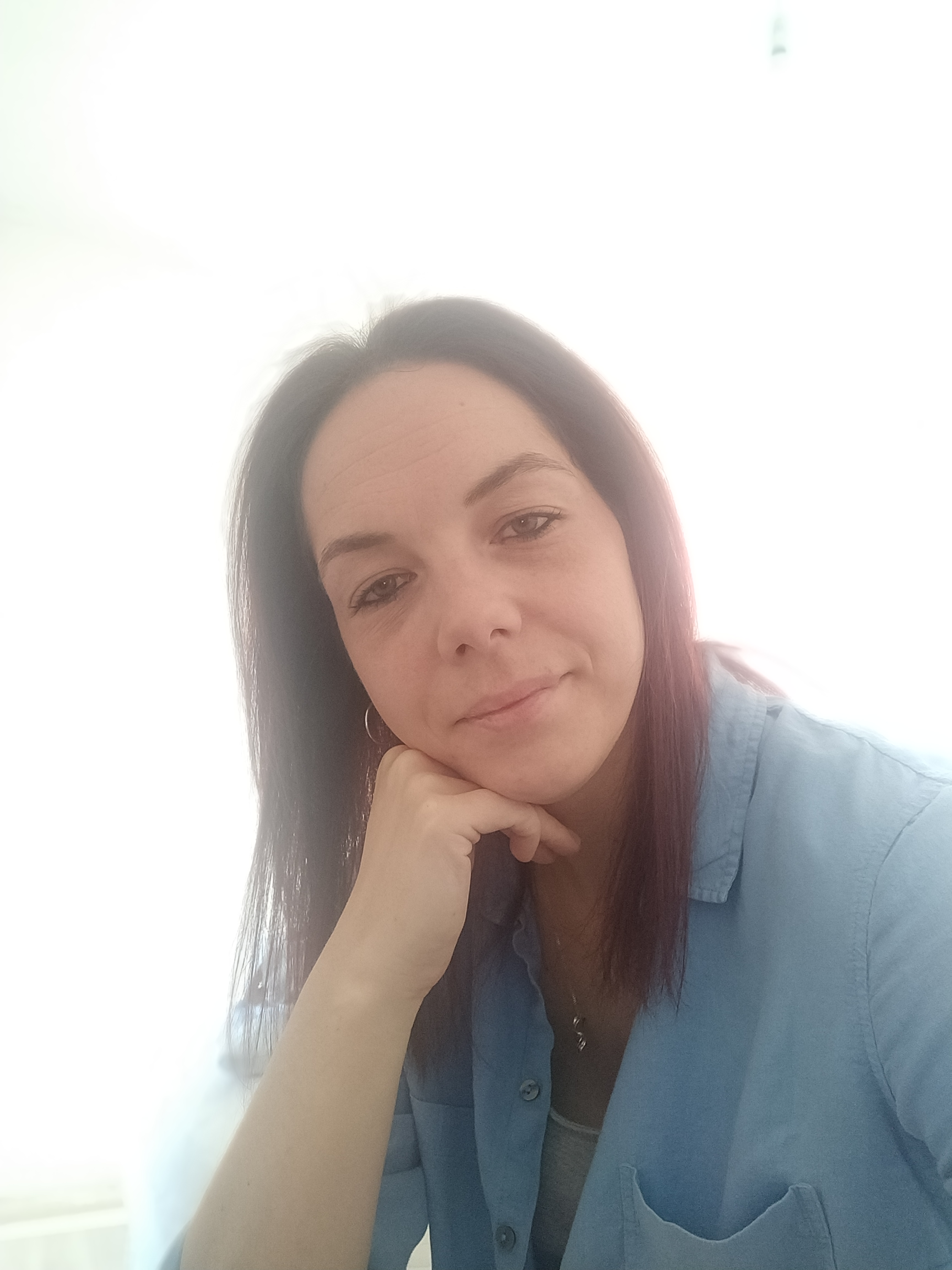 Caroline Latham, leaning on her right hand, wearing a blue blouse. 