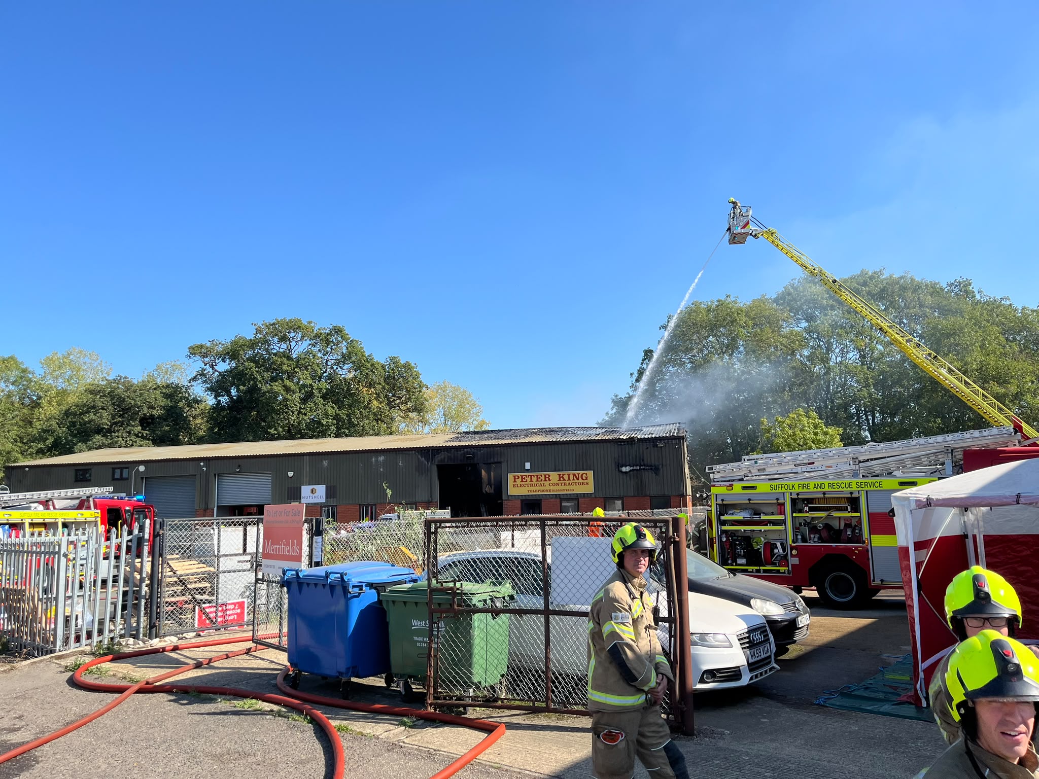 Firefighters on the ground outside and one on an aerial ladder at an industrial unit.
