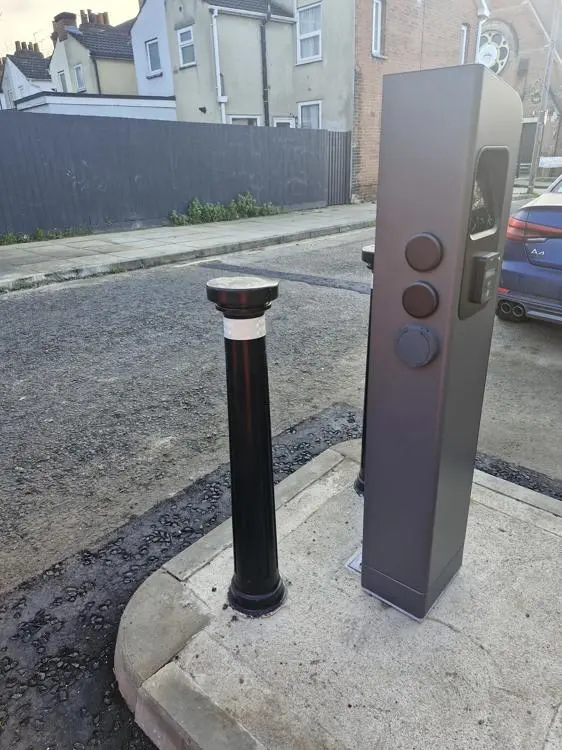 A charegepoint side on, with a picture of a socket to plug in a car. There is a bollard adjacent to the chargepoint.