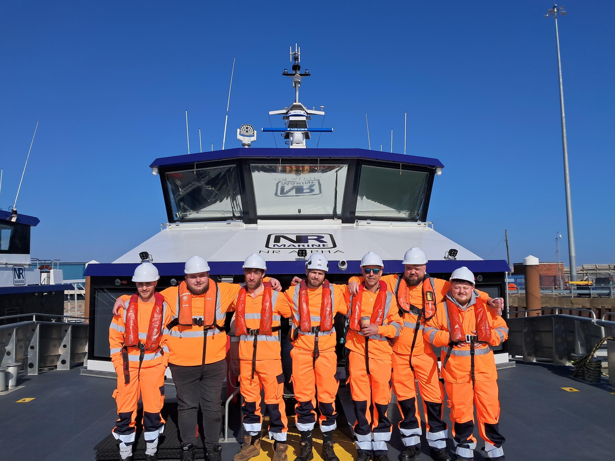 A Cohort of  7 Offshore Wind Vessel Support Skills Bootcamp Learners standing in a row onboard a vessel.