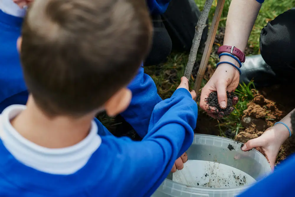 A school child helps put soil into the ground while tree planting