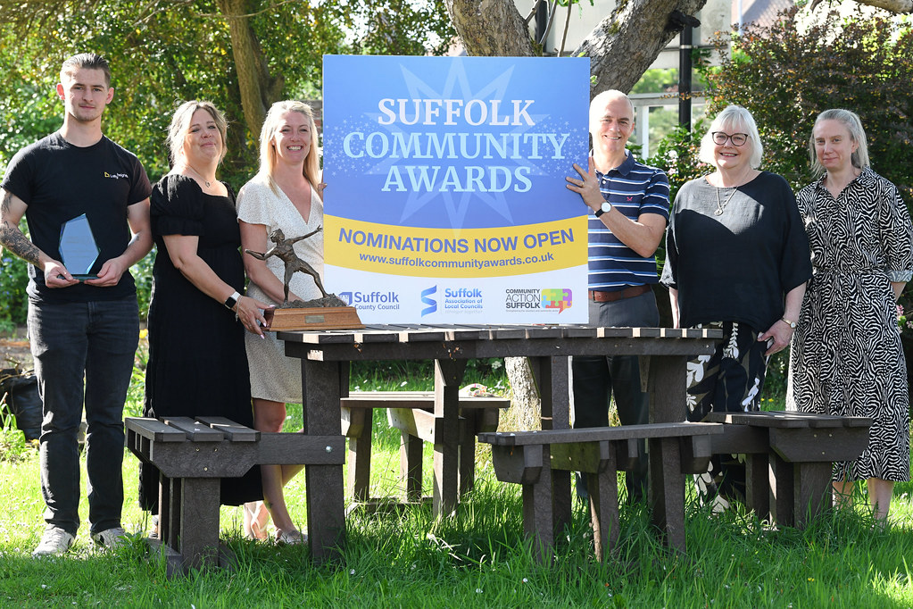 6 men and women round a picnic bench holding a sign saying Suffolk Community Awards nominations now open.