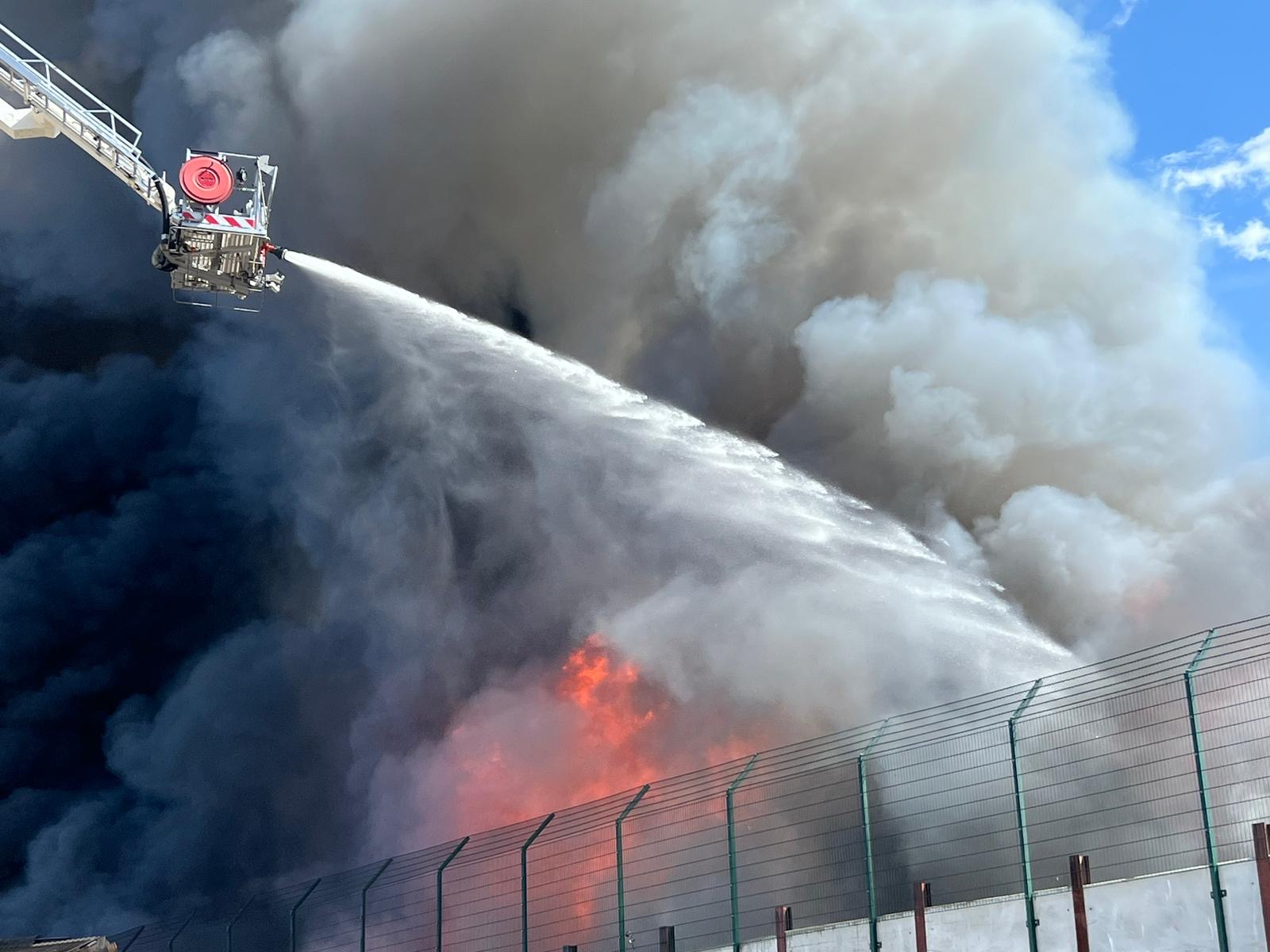 Water is sprayed on the fire at Sackers from an aerial ladder appliance, smoke and flames billow
