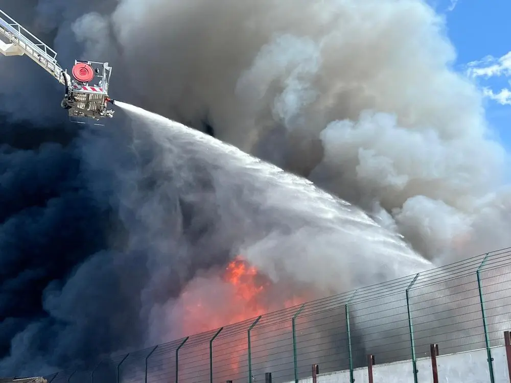 Water is sprayed on the fire at Sackers from an aerial ladder appliance, smoke and flames billow