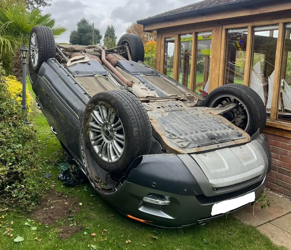 A car on its roof lying next to a house.