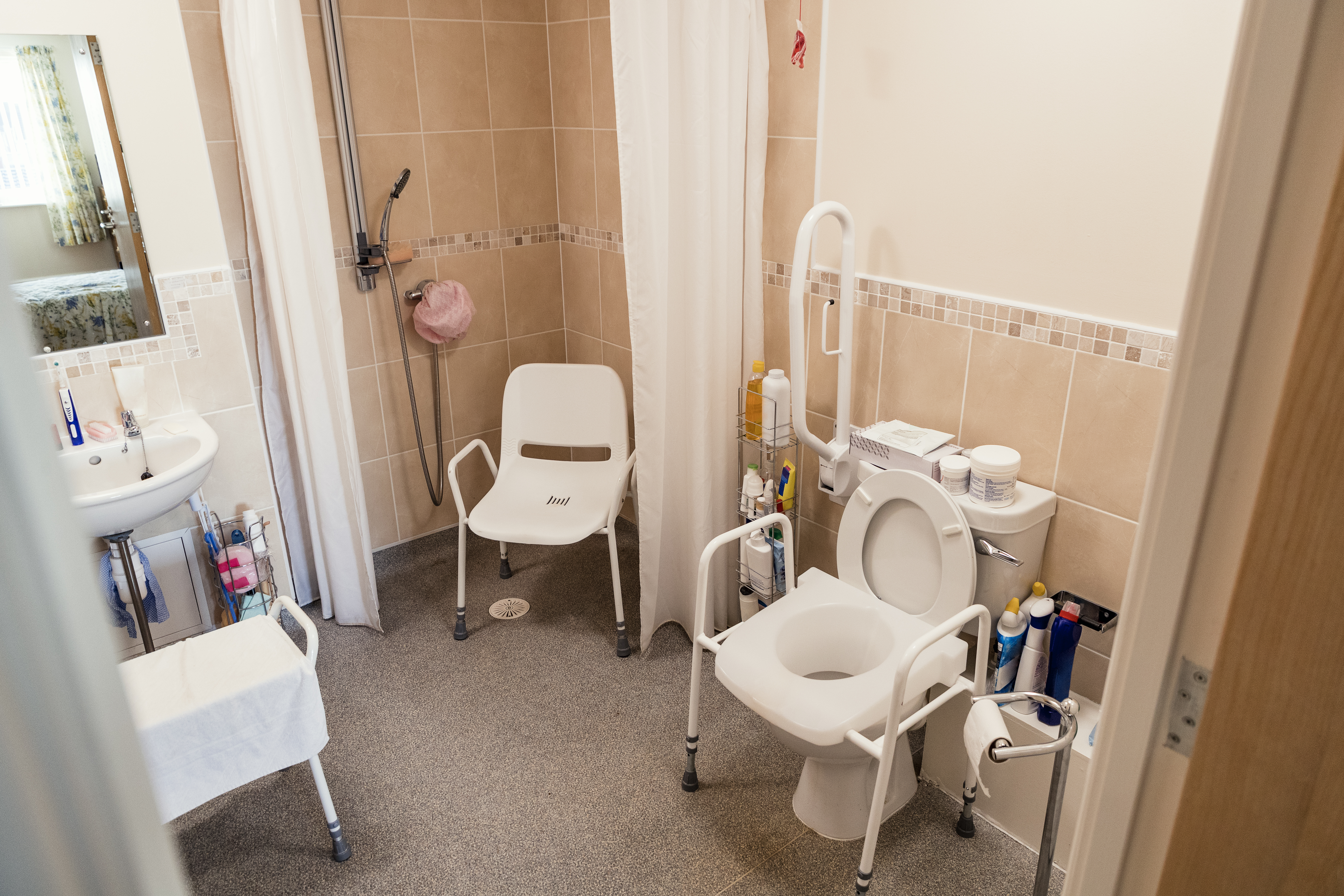 Bathroom with a shower chair, adapted raised toilet and grab rails.