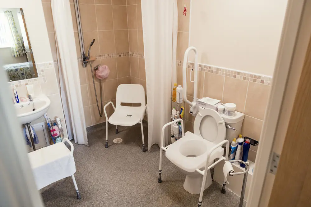 Bathroom with a shower chair, adapted raised toilet and grab rails.