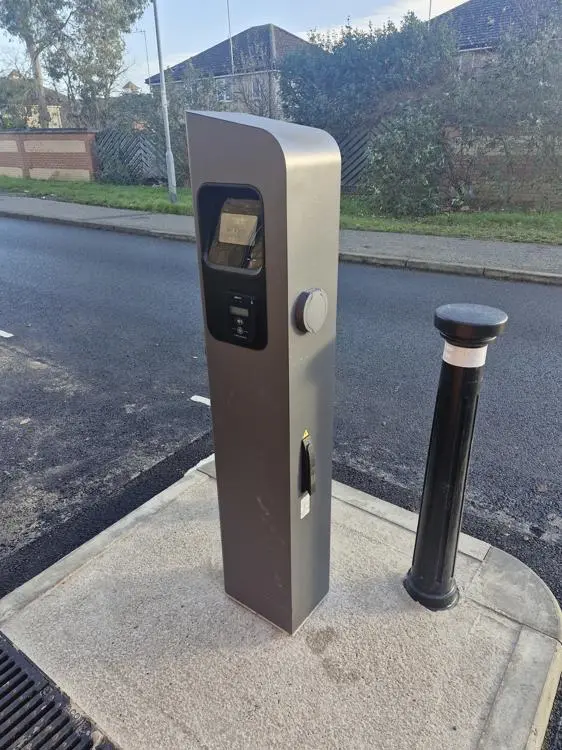A chargepoint by the side of the road with a bollard to protect it.