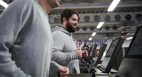 Two men in grey jumpers in the gym jogging on running machines