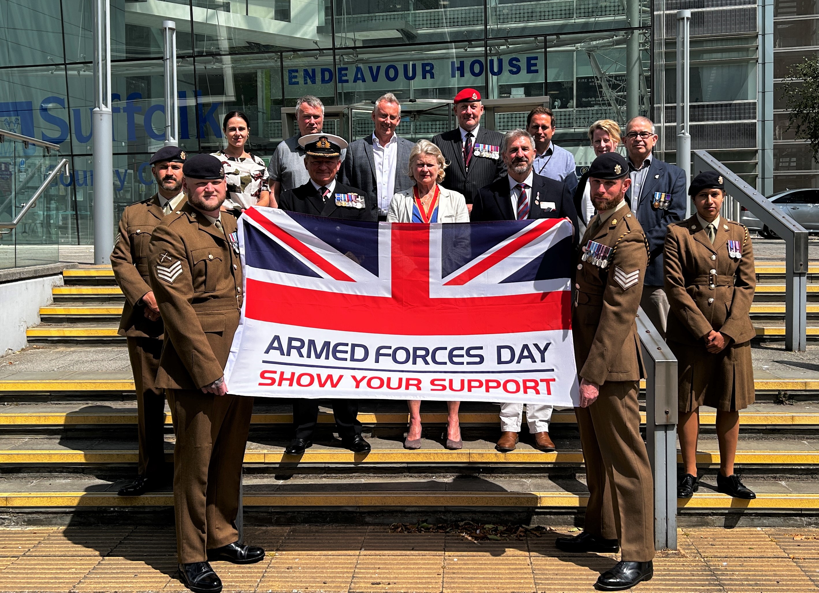 Soldiers, sailors and civilians with the Armed Forces Day flag on the steps of Endeavour House