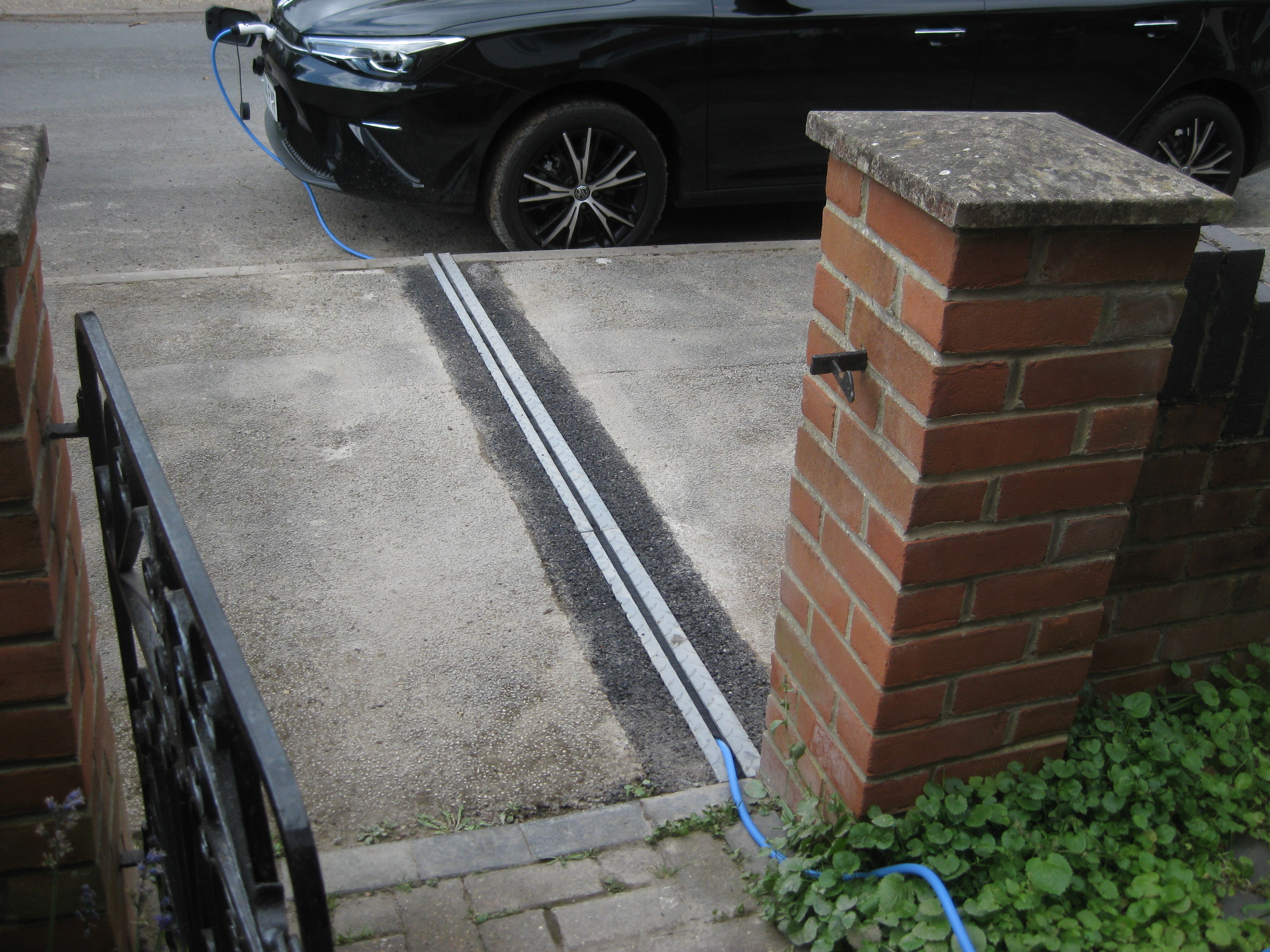 A black car on a road, with a charging channel running through a gully on the pavement. 