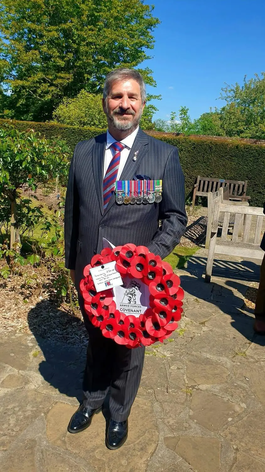 Andrew Smith in a suit with medals and holding a poppy wreath.