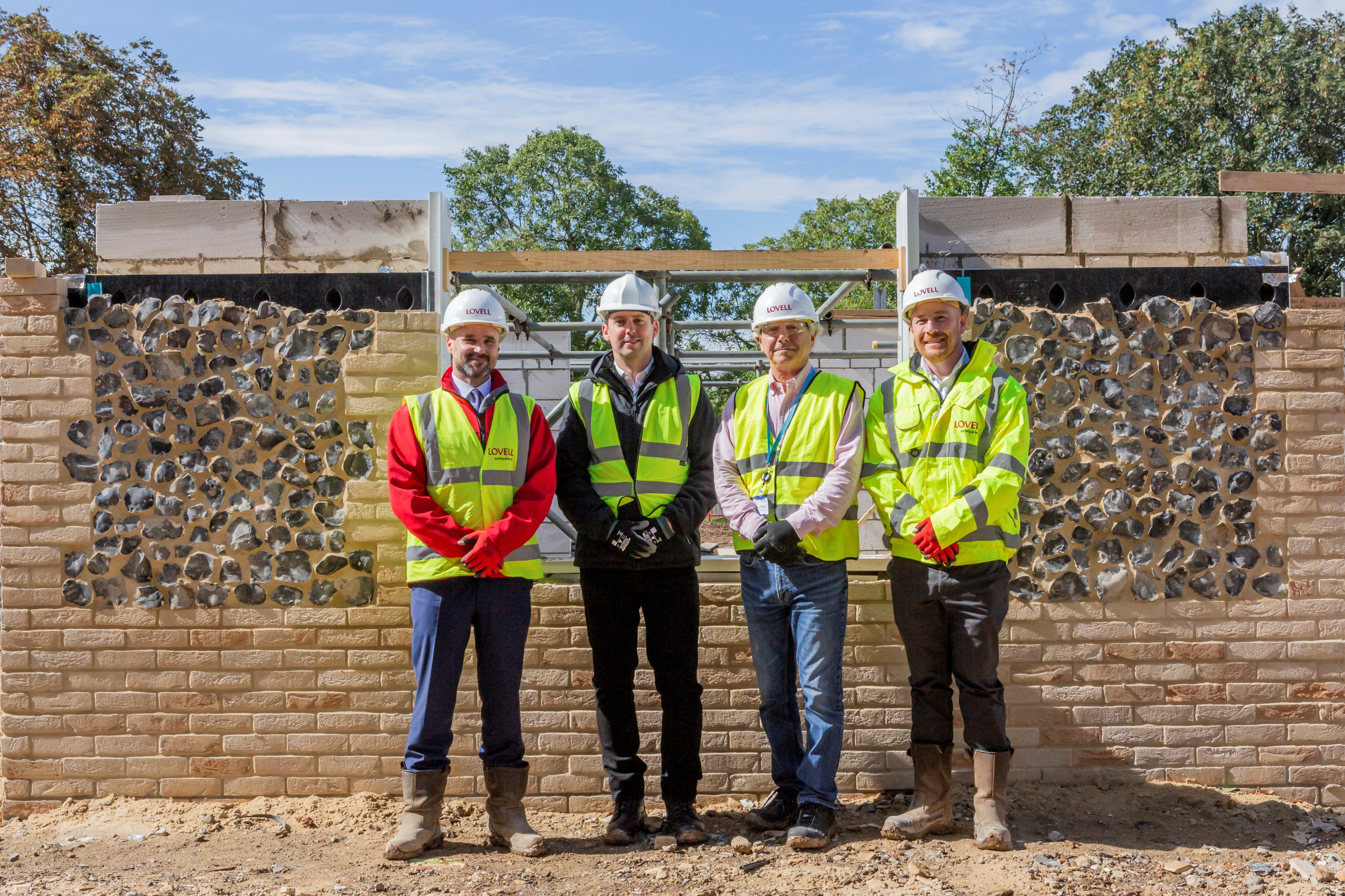 four people in hi vis clothing pose for a photo outside the construction of a house