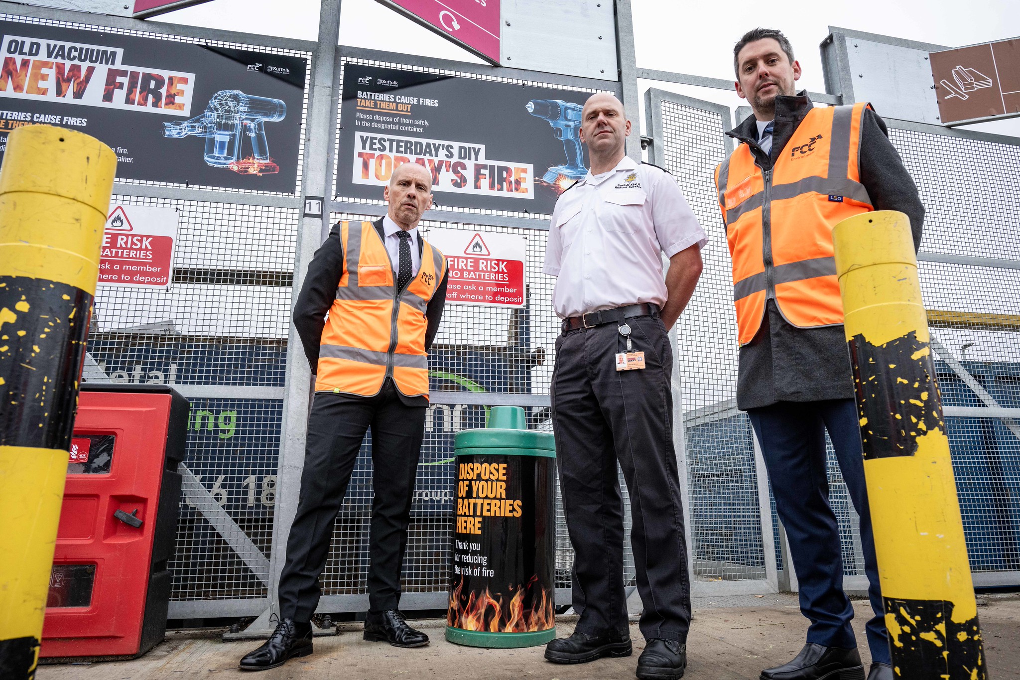 Three people stand in front of new battery campaign branding at a recycling centre