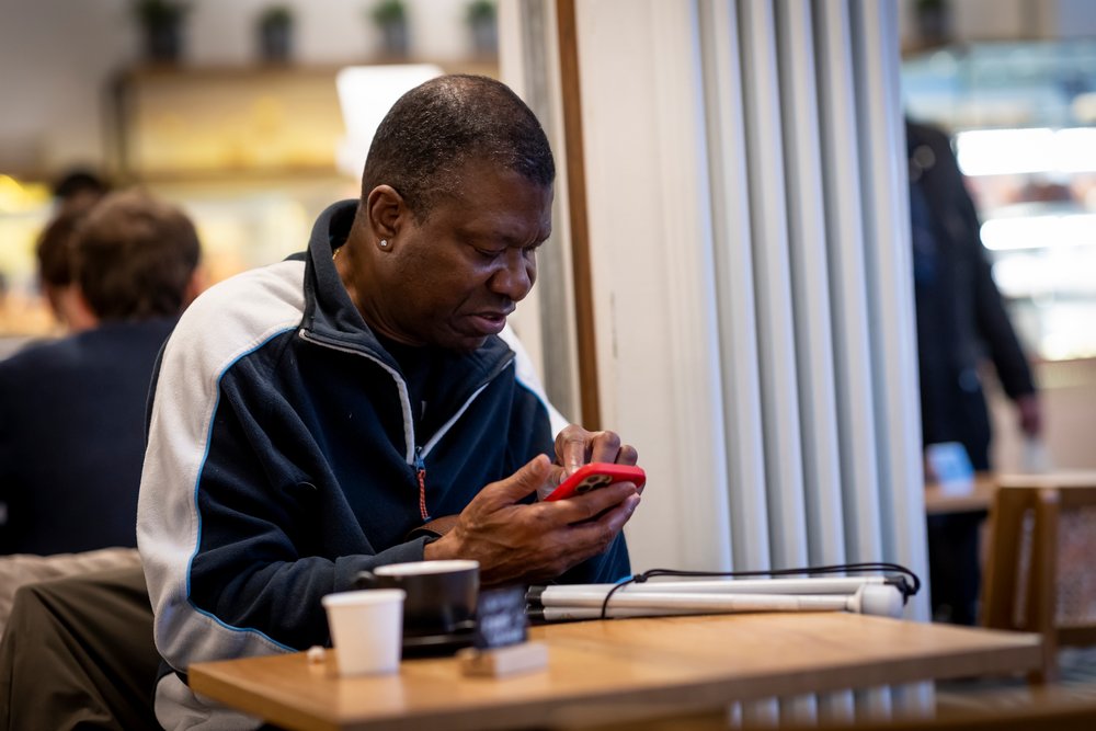 Adult black man sitting in a cafe typing on his phone