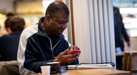 Adult black man sitting in a cafe typing on his phone
