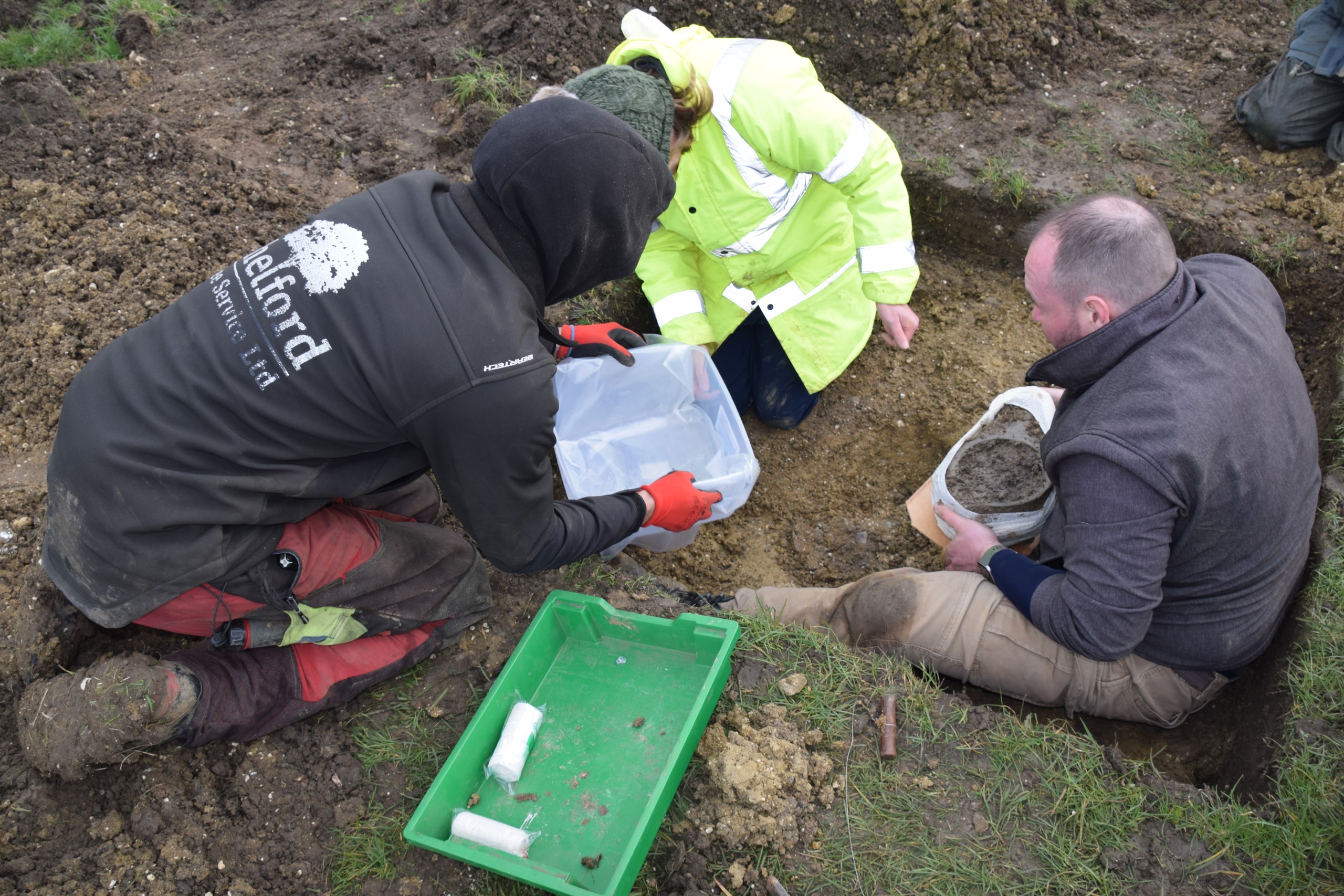 A team of three people carefully block-lift the pan from the ground