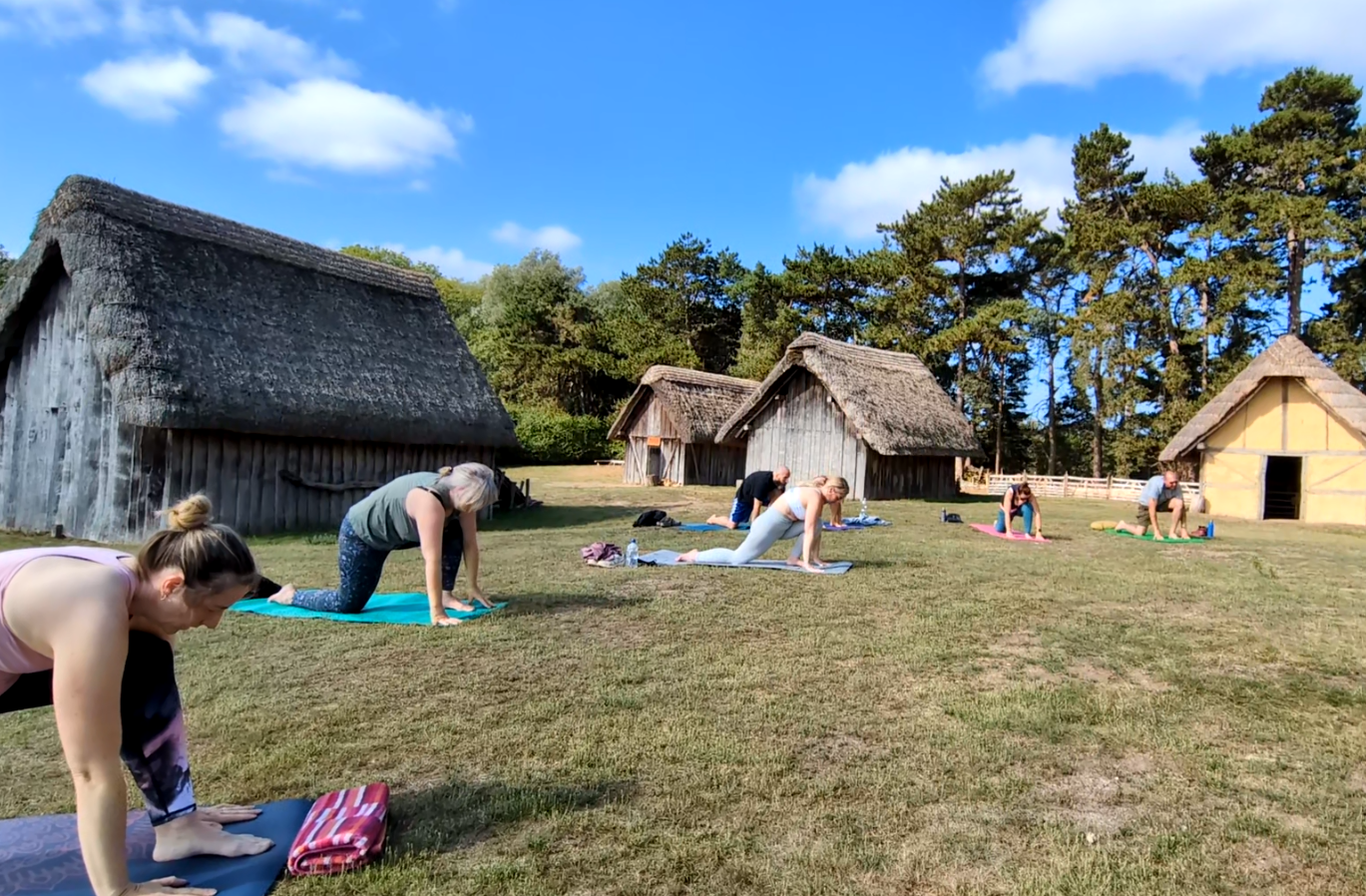 a group of people practising yoga outside in front of thatched huts