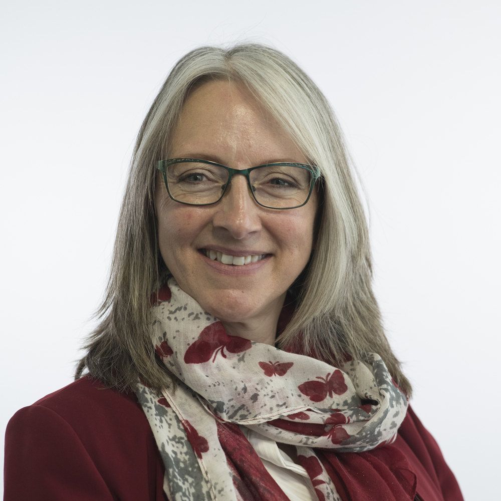 Caroline Topping, councillor, wearing glasses, red jacket, a butterfly patterned scarf, hair is cut past the shoulders. 