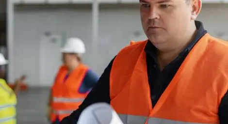 A man wearing construction clothes is looking at a drawing of some building designs.
