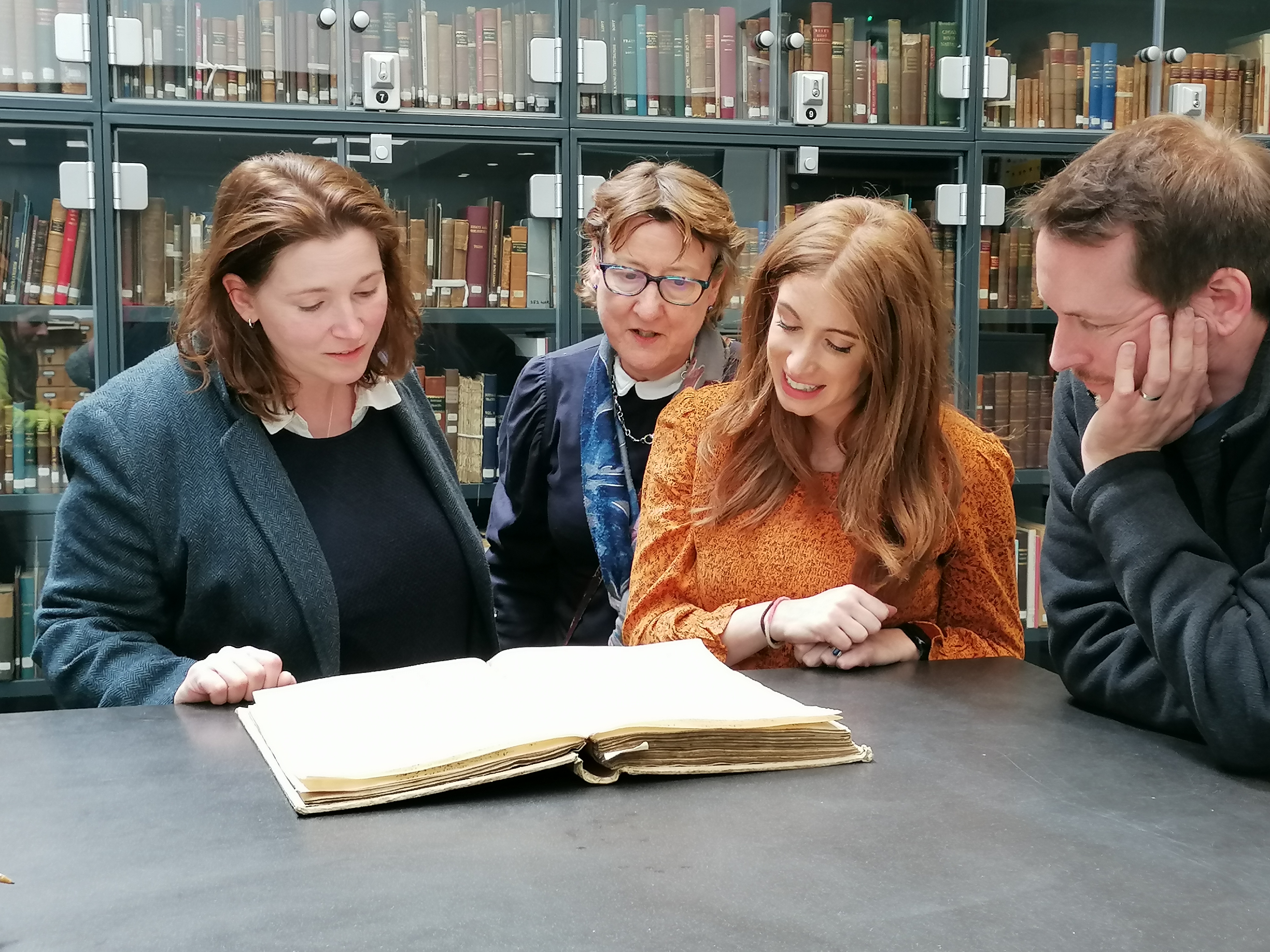 A group of people looking at a book of historical records 