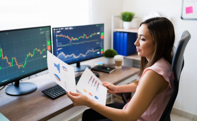 A data technician is studying graphs whilst sitting in front of two computer screens.