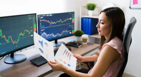 A data technician is studying graphs whilst sitting in front of two computer screens.