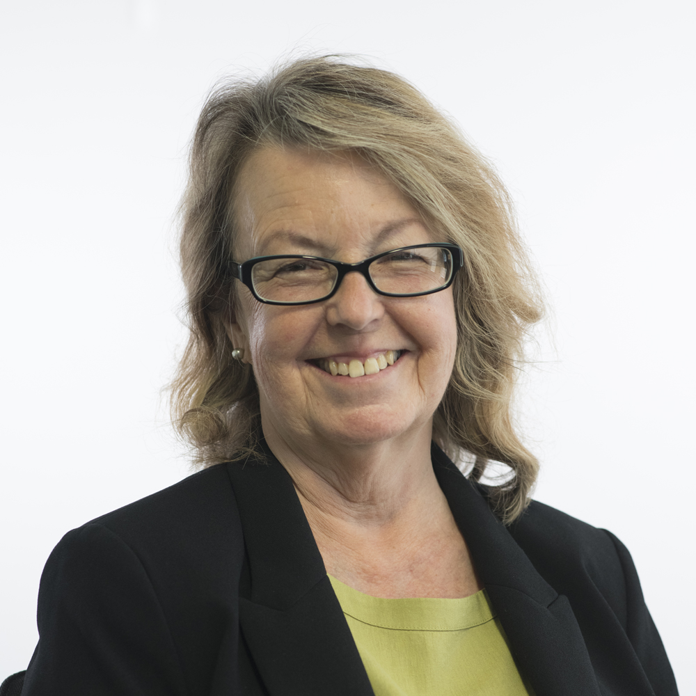 Image of Debbie Richards, wearing a lime green top and black jacket, black glasses with blonde hair to the shoulders. 