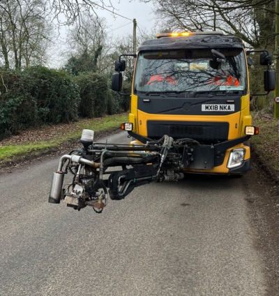 Yellow dragon patcher vehicle with two people in fluorescent orange coats in the front. 