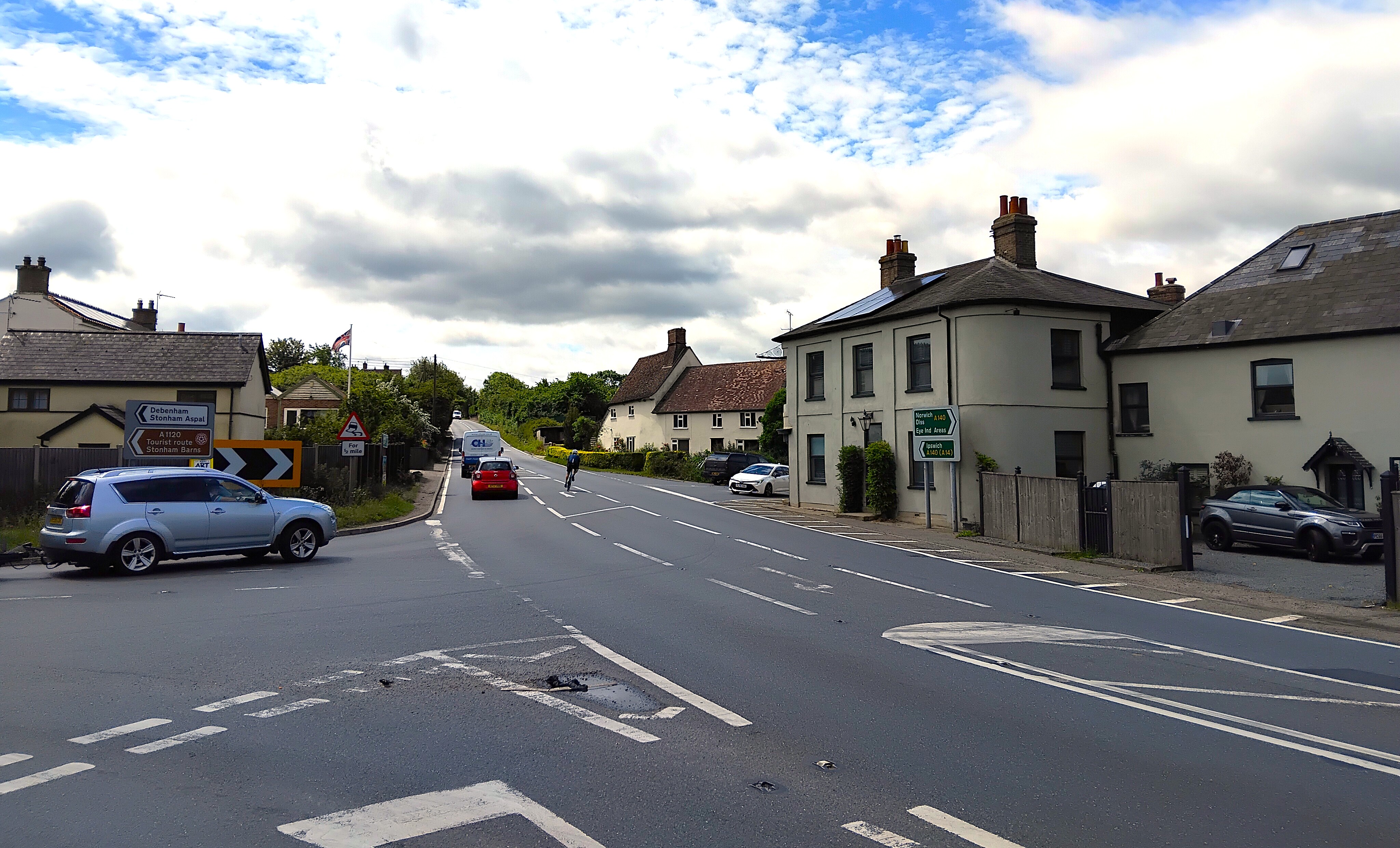 Cars and a cyclist on a staggered crossroads junction.