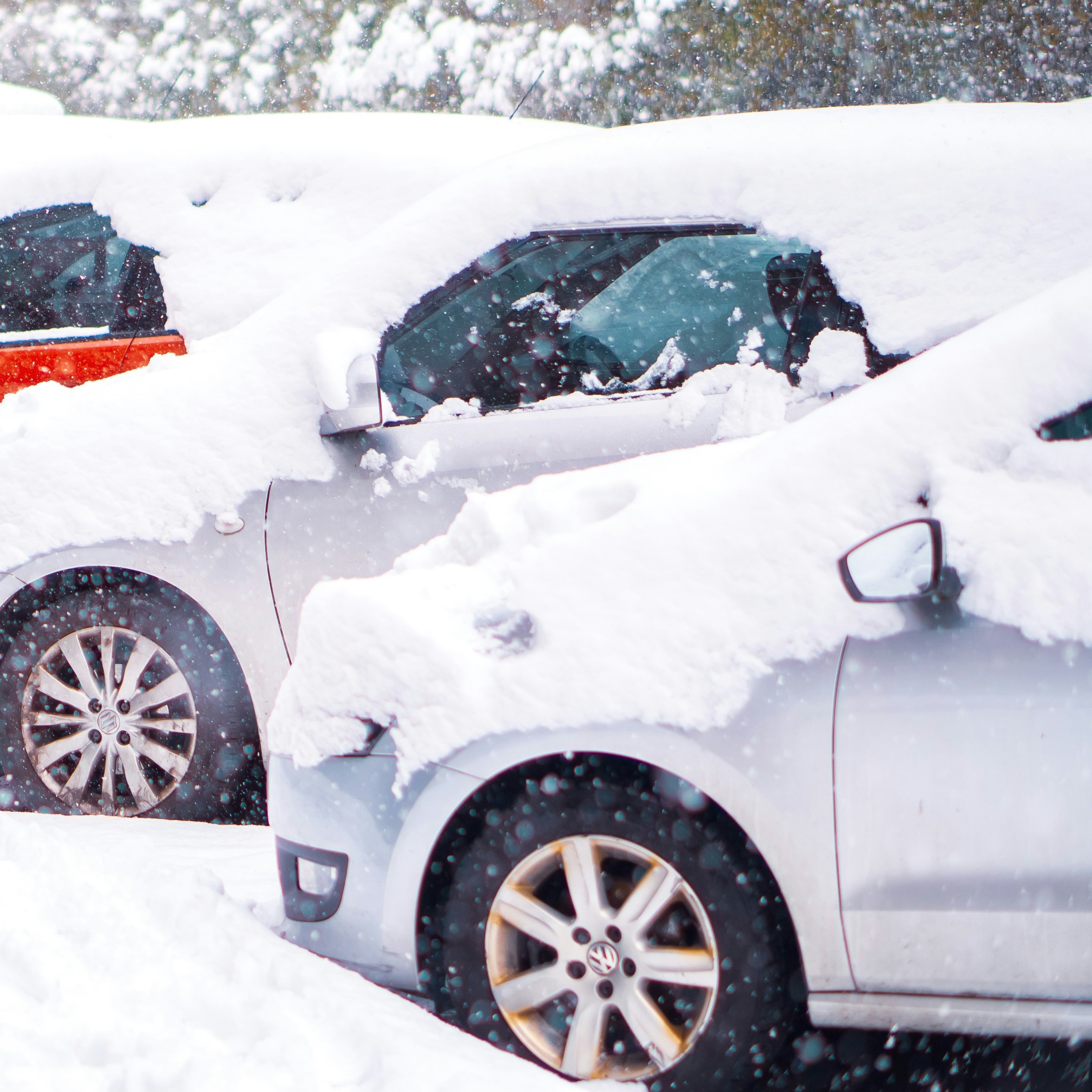 Two or three cars parked in a row, covered in heavy snow. 