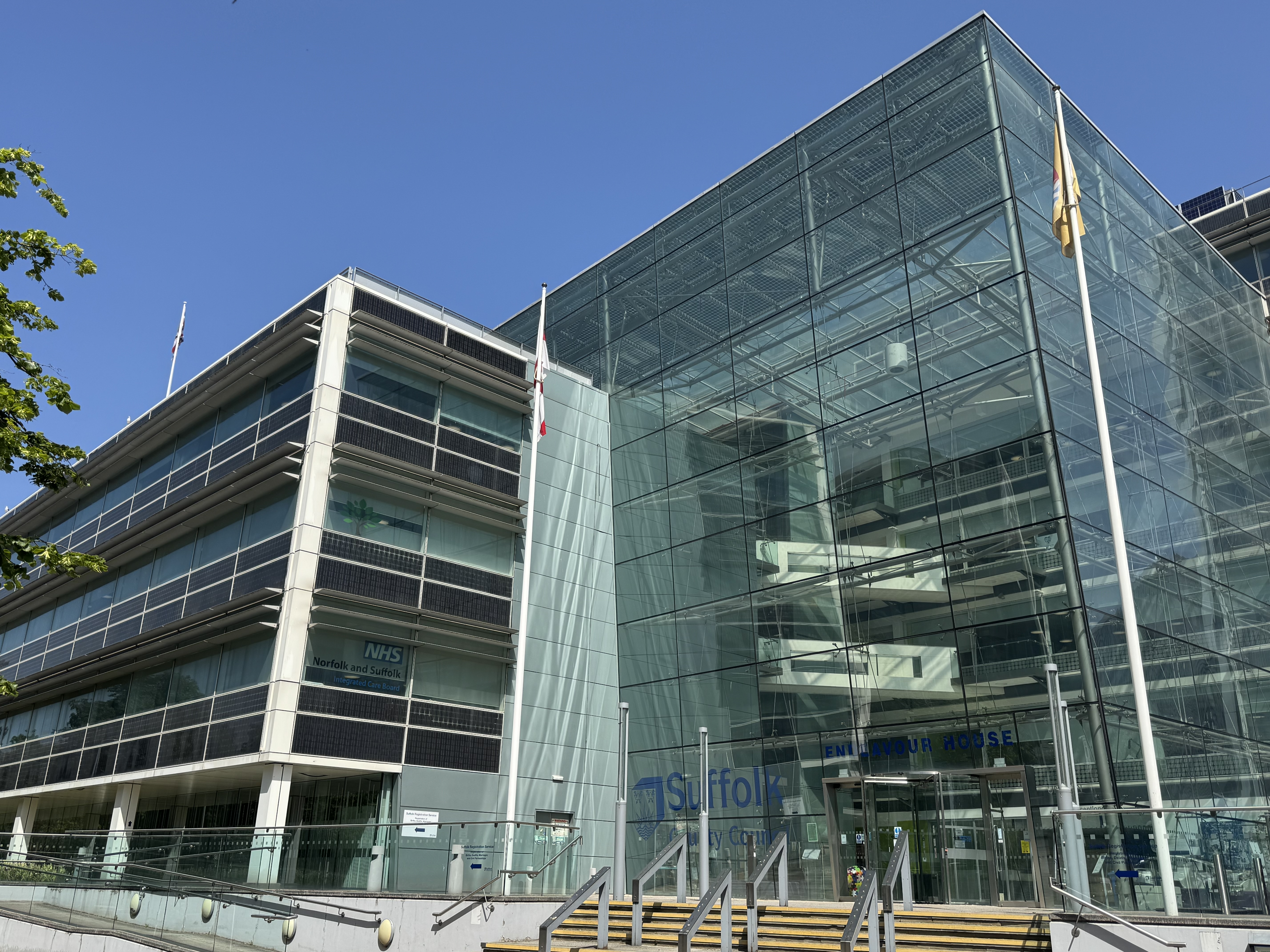 Endeavour House, a large glass commercial building in Ipswich in the sunshine, flying three flags.