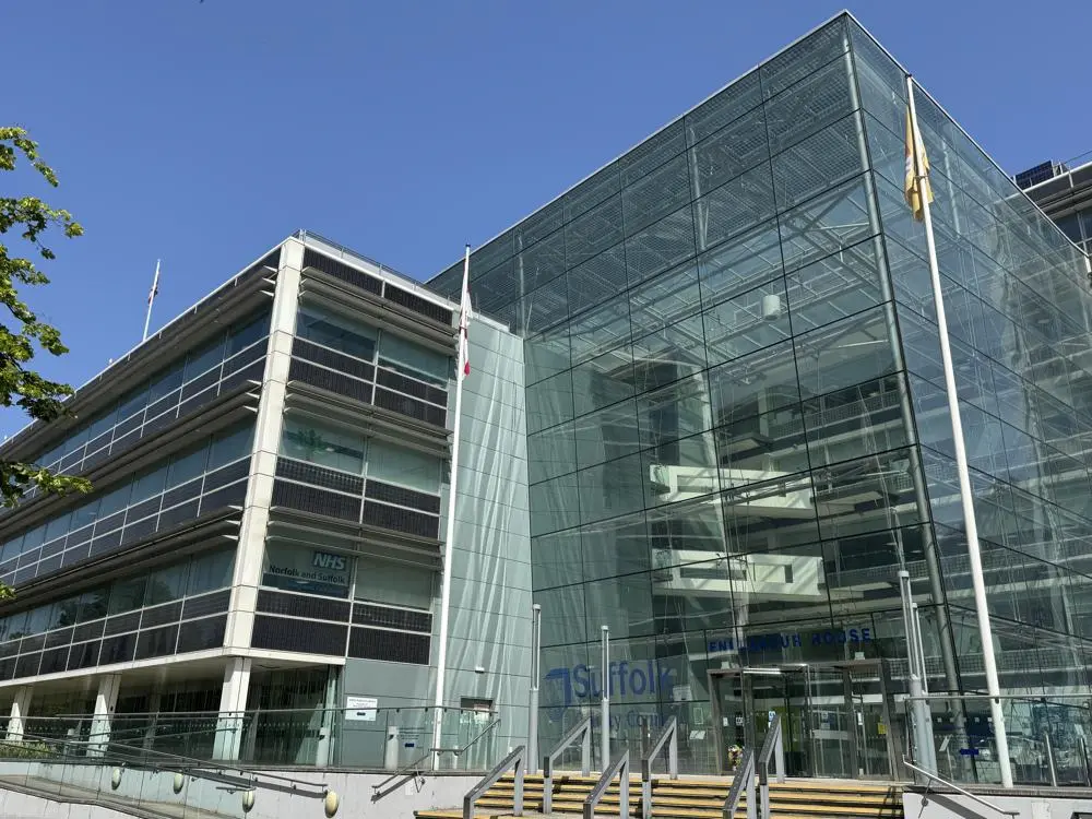 Endeavour House, a large glass commercial building in Ipswich in the sunshine, flying three flags.
