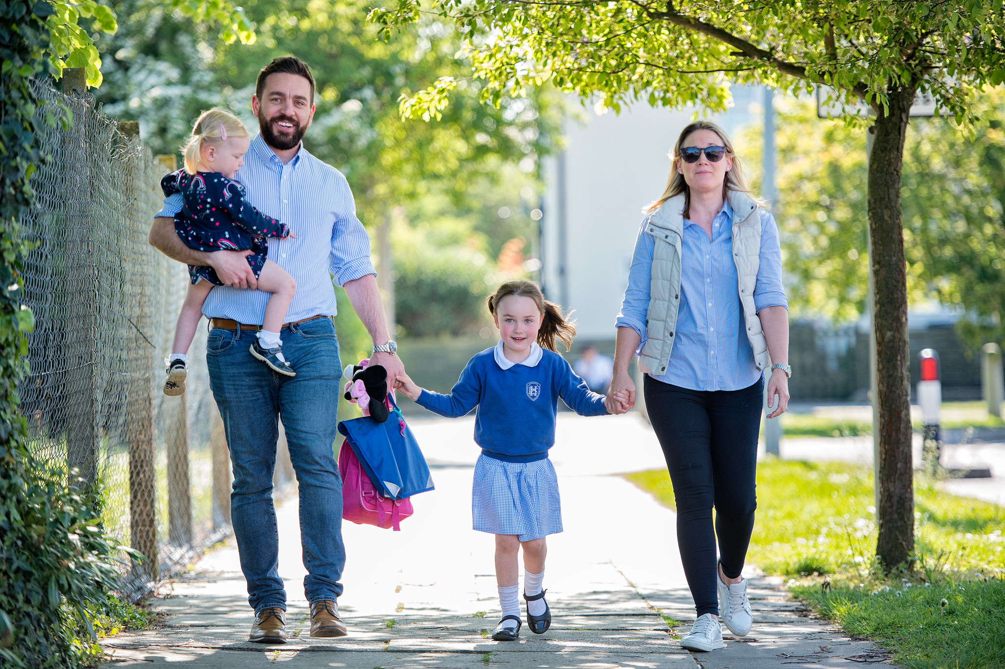 A couple with a toddler walk a small child to school on a sunny day