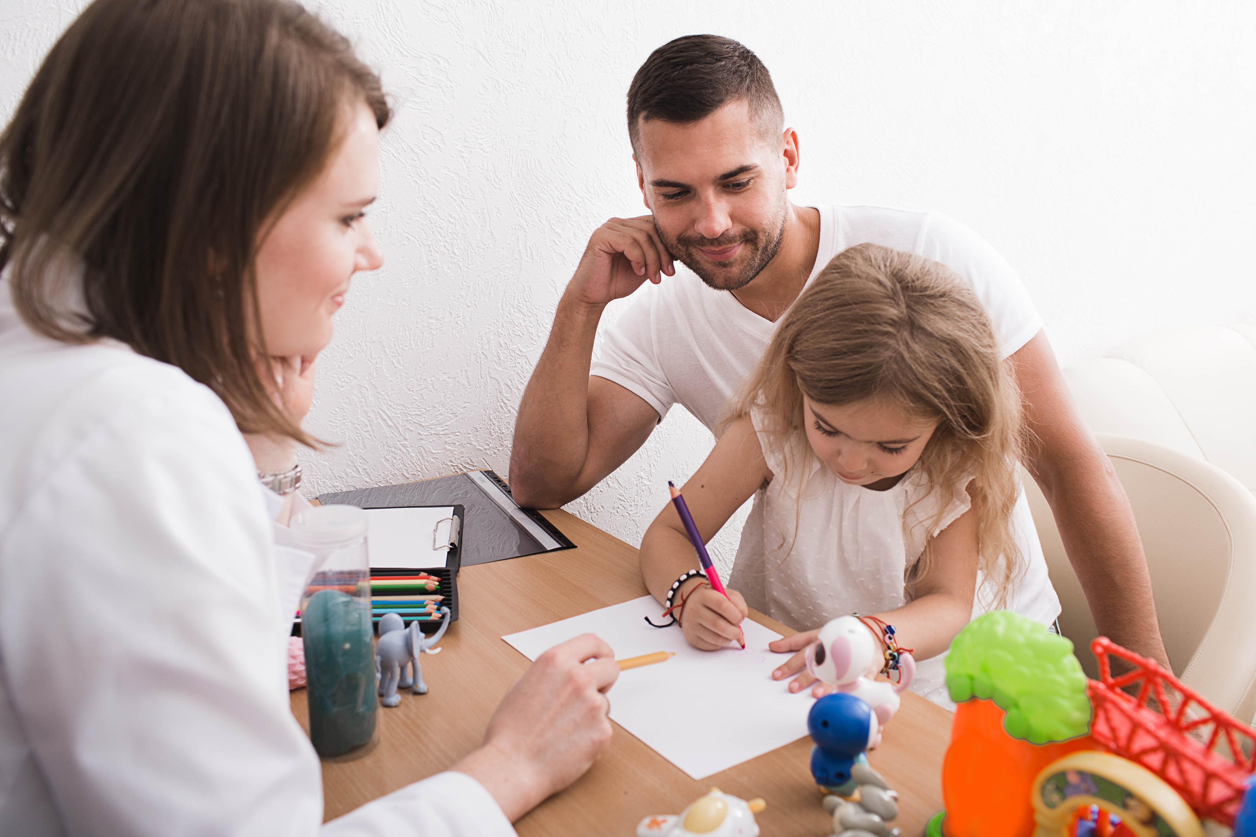 2 adults watching child drawing on a piece of paper