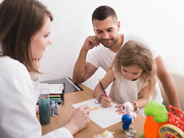 2 adults watching child drawing on a piece of paper