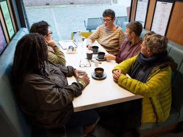 Five women over 50 chat with coffee in a coffee shop