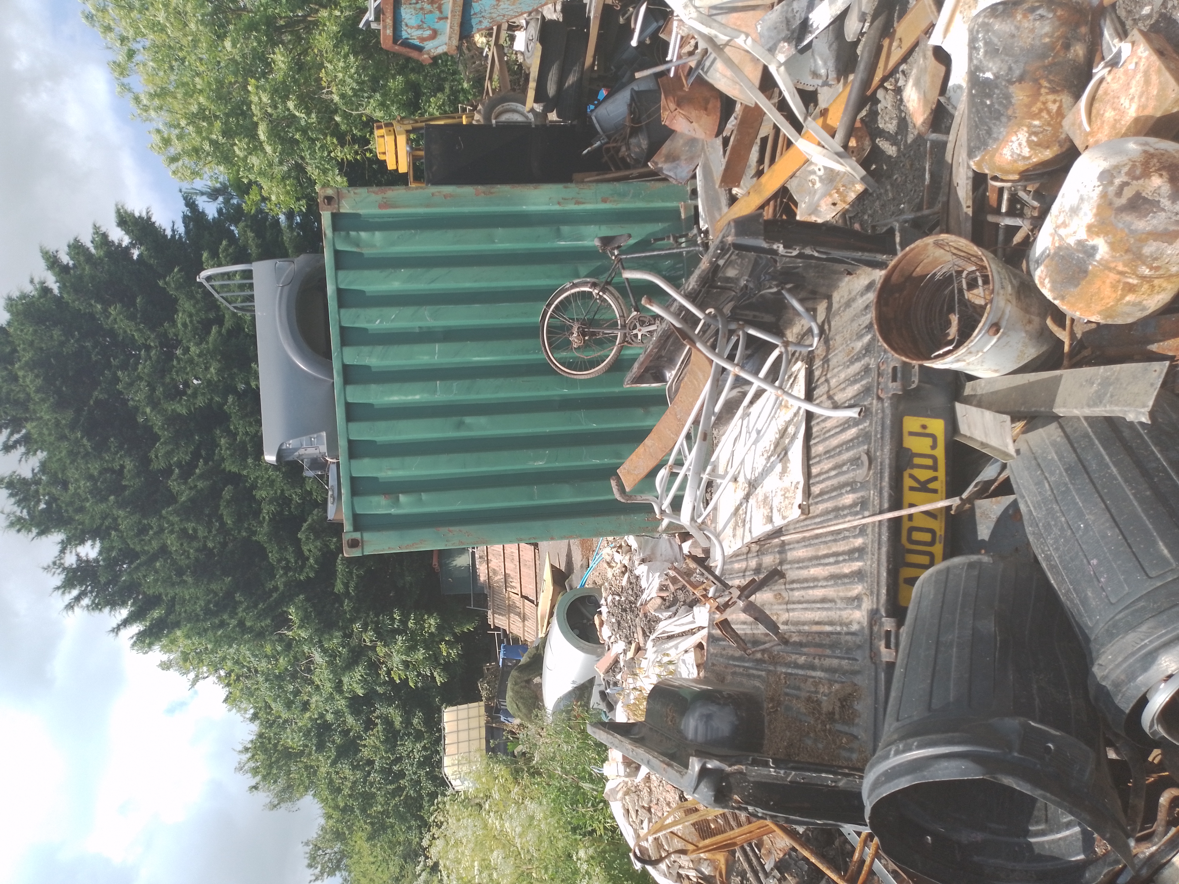 a huge pile of waste on green land, including a container, bins, van trailer, wood and scrap metal