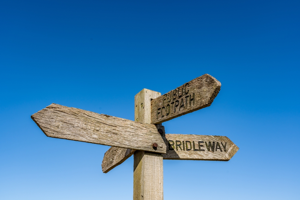 A wooden footpath sign stands in front of a clear blue sky