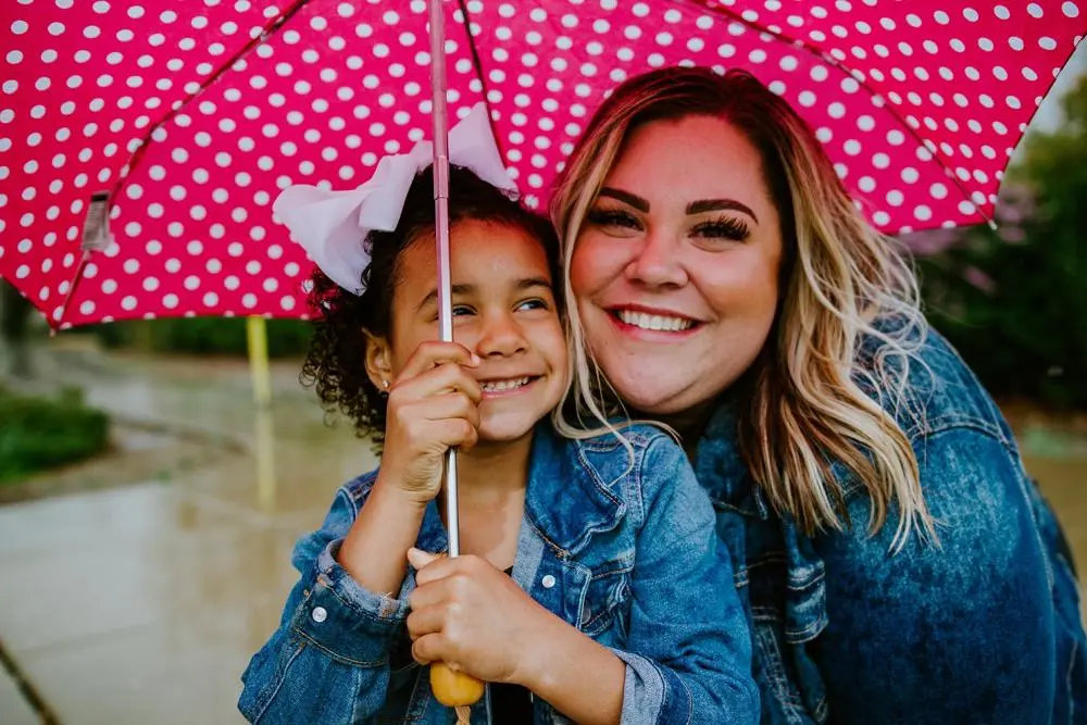 Foster mother and daughter smiling and holding a pink polka dot umbrella