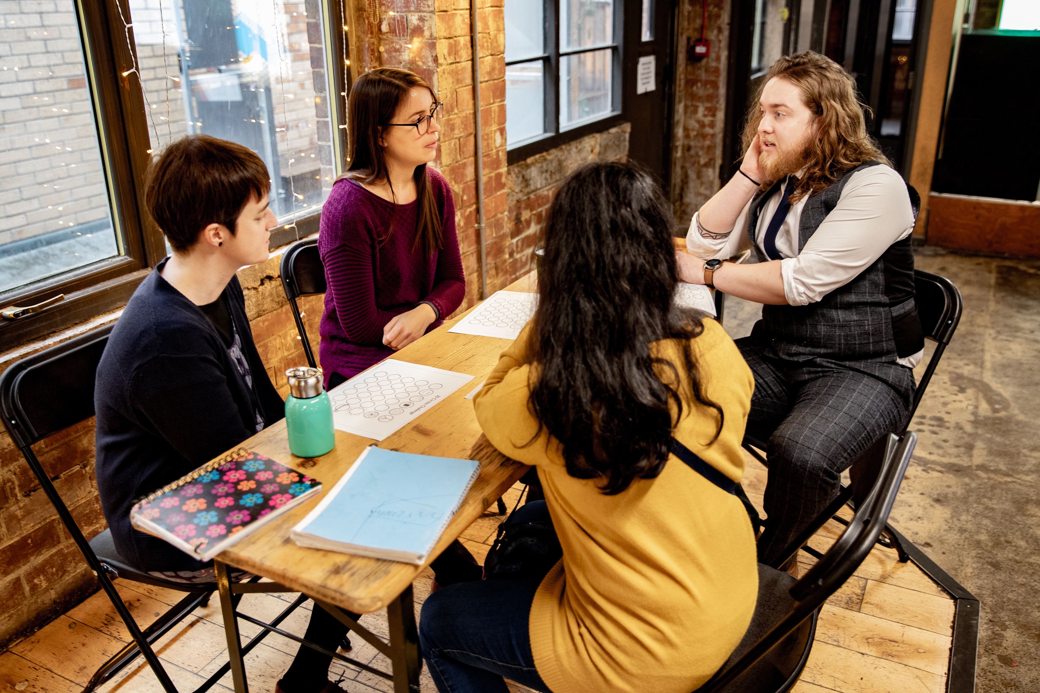 Four people are sitting around a table talking with notepads on the table