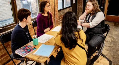 Four people are sitting around a table talking with notepads on the table