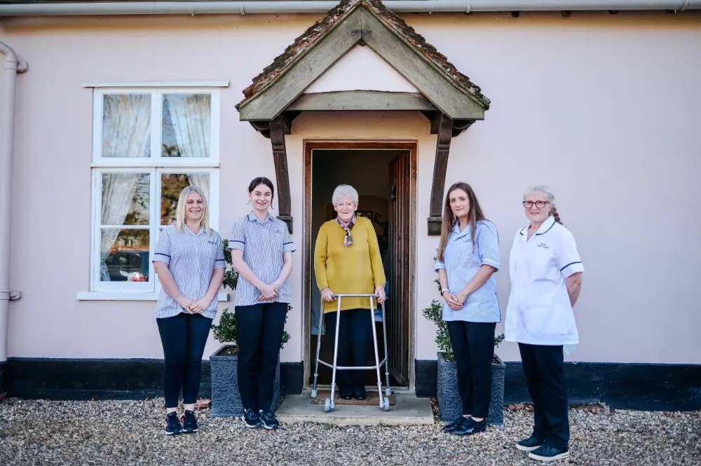 A group of carers in front of an older persons house who is standing in the middle of the photo.